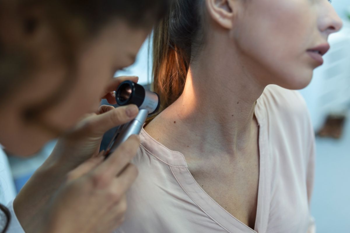 A dermatologist examines the skin on a woman's neck