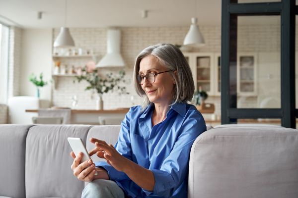 A woman sits on a couch looking at her phone, using the Patient Portal