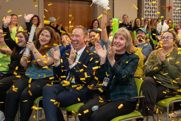 A room full of people sitting on green chairs clap in celebration as confetti falls around them